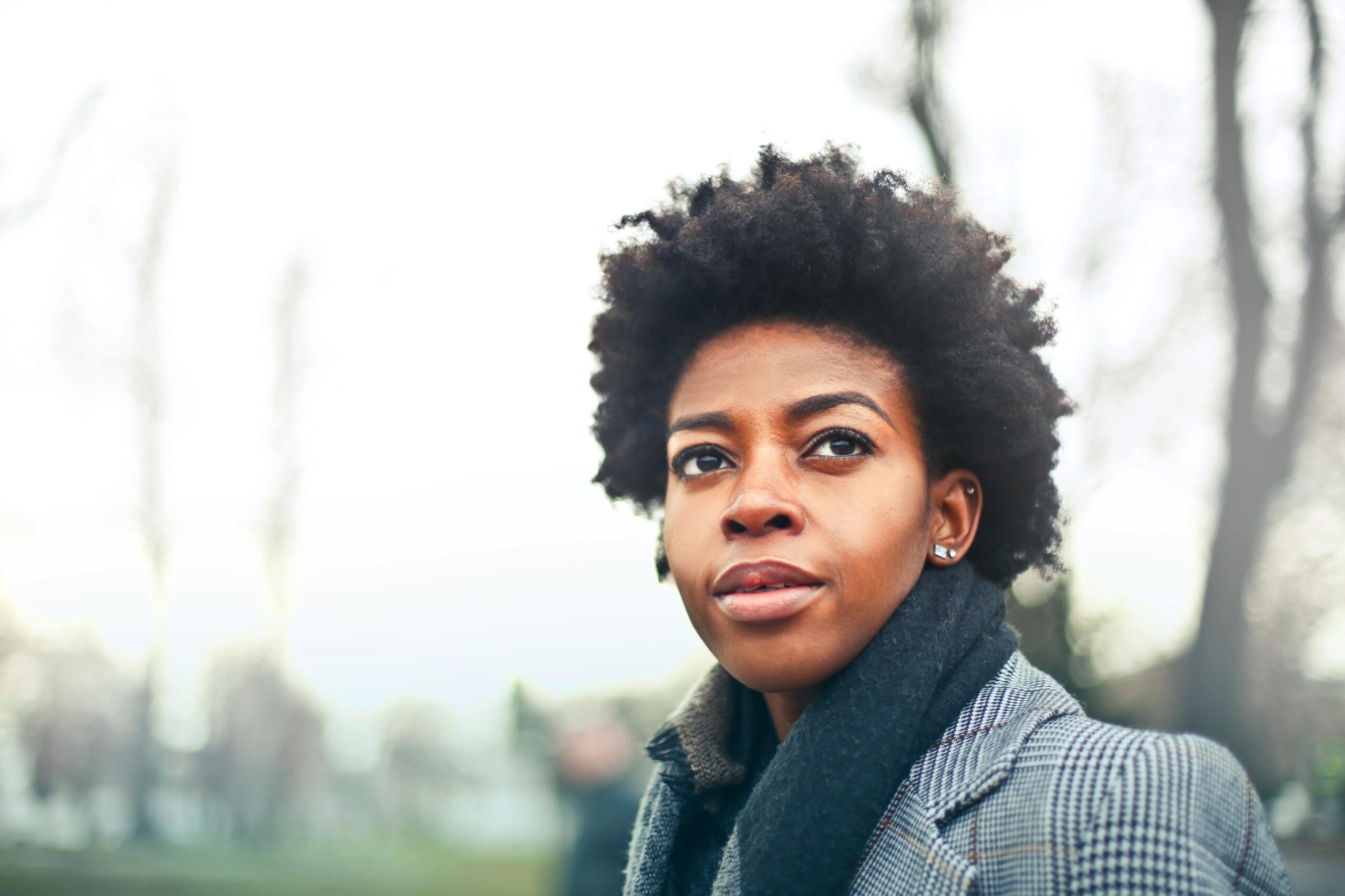 A fashionable black woman with an afro hairstyle in a winter coat poses outdoors in Budapest park.